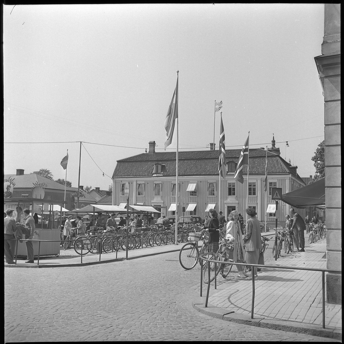 Norska och svenska flaggor hissade vid Stora torget och Rådhuset, 4 juni 1950. Kiosk med försäljning av Tyrol-glass ligger i hörnet av torget.