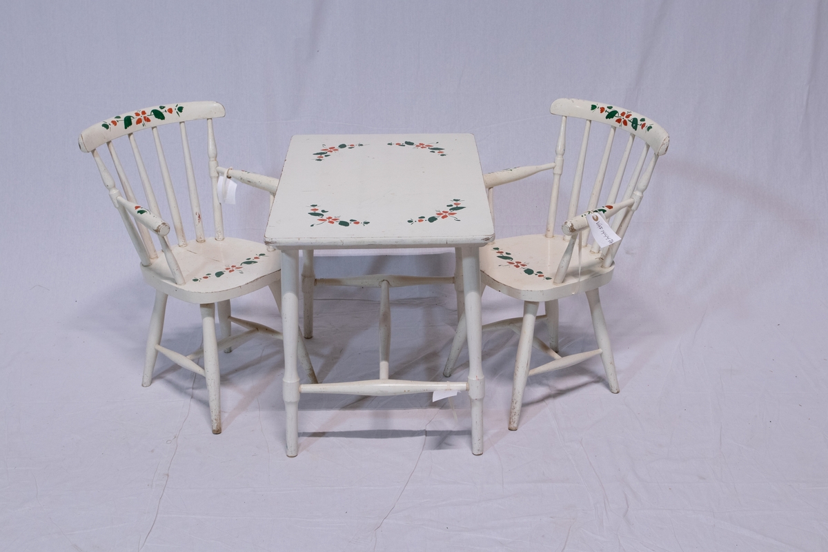 To barnestoler og bord. Hvitmalt. Enkel malt dekor i grønt og rødt på alle delene. Skal ligne blomstermotiv. Rektangulært bord med dreide ben. Stolene er pinnestoler med armlener.