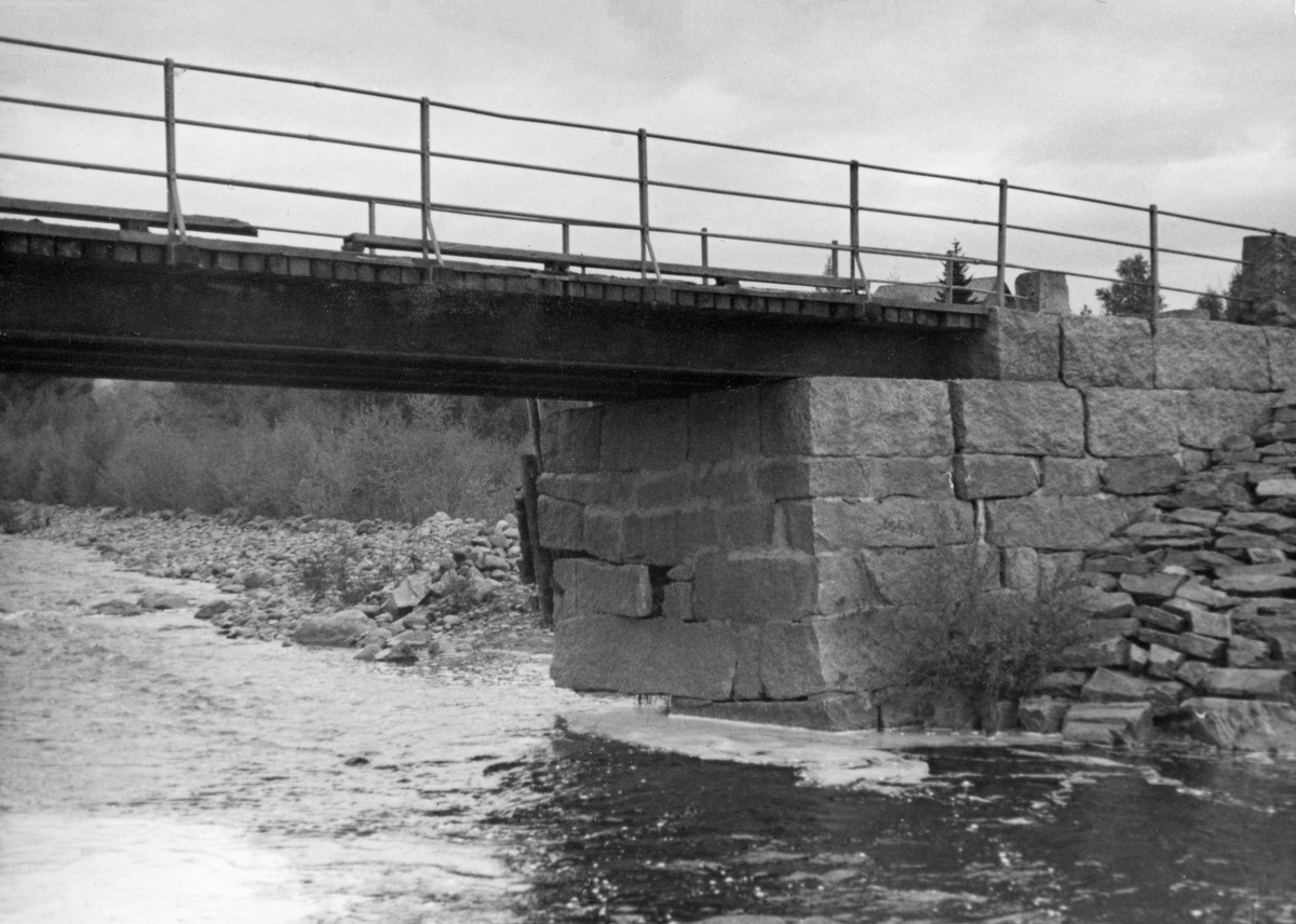 Detalj fra Knapper bru i Nord-Odal, Hedmark, fotografert i 1936. Bildet er tatt mot et av landkarene, som later til å være en kistemurkonstruksjon, lagd av grov, kvadret naturstein. Dette var ei platebru med trebane, båret av kraftige ståldragere og med jernrekkverk langs ytterkantene. Det foruroligende later til å ha vært at at elva hadde gravd under ytterkanten av brukaret, slik at overliggende murverk manglet understøtning. Karet på motsatt elvebredd later til å ha stått på berggrunn, så her ser man ikke ut til å ha hatt samme problem.