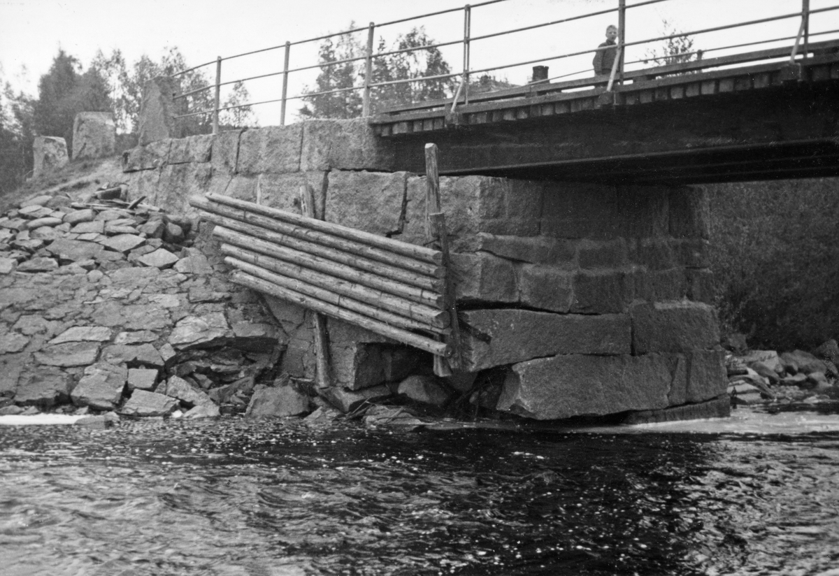 Detalj fra Knapper bru i Nord-Odal, Hedmark, fotografert i 1936. Bildet er tatt mot et av landkarene, som later til å være en kistemurkonstruksjon, lagd av grov, kvadret naturstein, en mur som på den sida fotografen har stått var forblendet med en skjerm av rundtømmer. Dette var ei platebru med trebane, båret av kraftige ståldragere. Det foruroligende later til å ha vært at at elva hadde gravd under ytterkanten av brukaret, slik at overliggende murverk manglet understøtning. Da fotografiet ble tatt var det en gutt som befant seg oppå brua,.