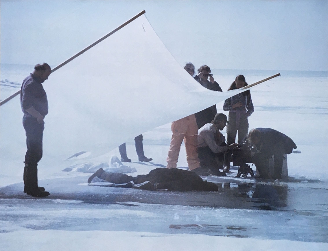 Ett filmteam på en is. De filmar en man som ligger på magen på isen. Ovanför honom ett stort ljust tygstycke som skuggar honom något.