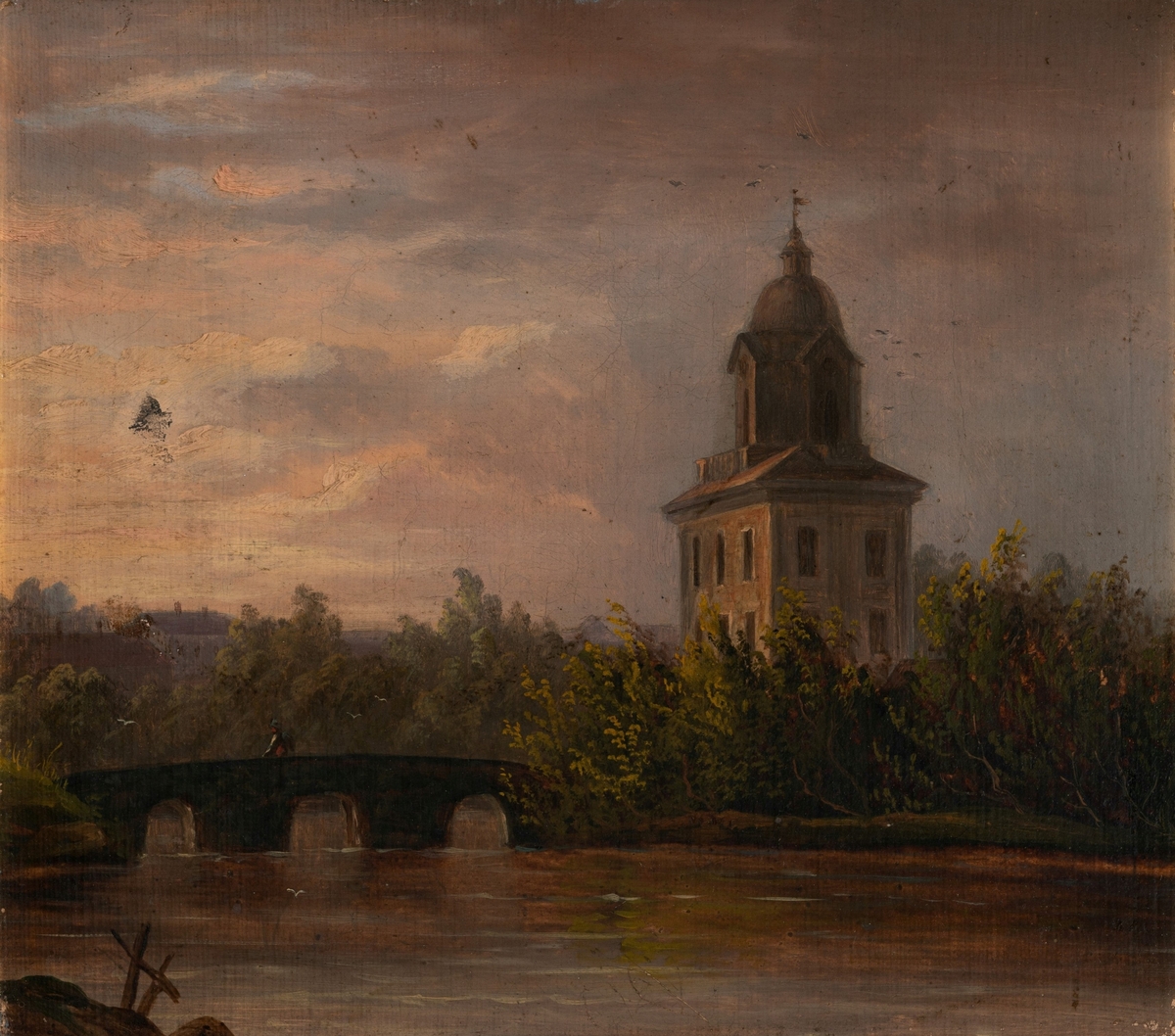 Kirketårn stikker opp blant løvtrær i en by. En bro i forgrunn krysser en elv. Kveldstid med rødlige skyer