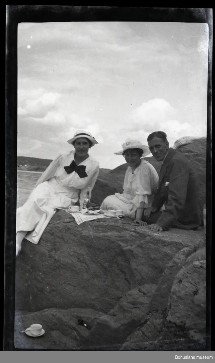 Tre person sittandes på en klippa vid havet.