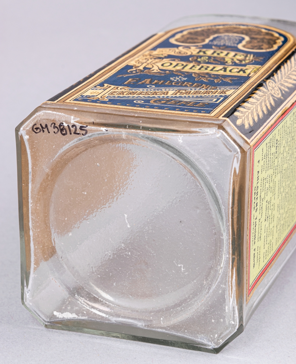 Glasflaska för bläck, fyrkantig med kork. Etikett på tre sidor, "Skrif- & Kopiebläck", "F. Ahlgrens Tekniska Fabrik Gefle".