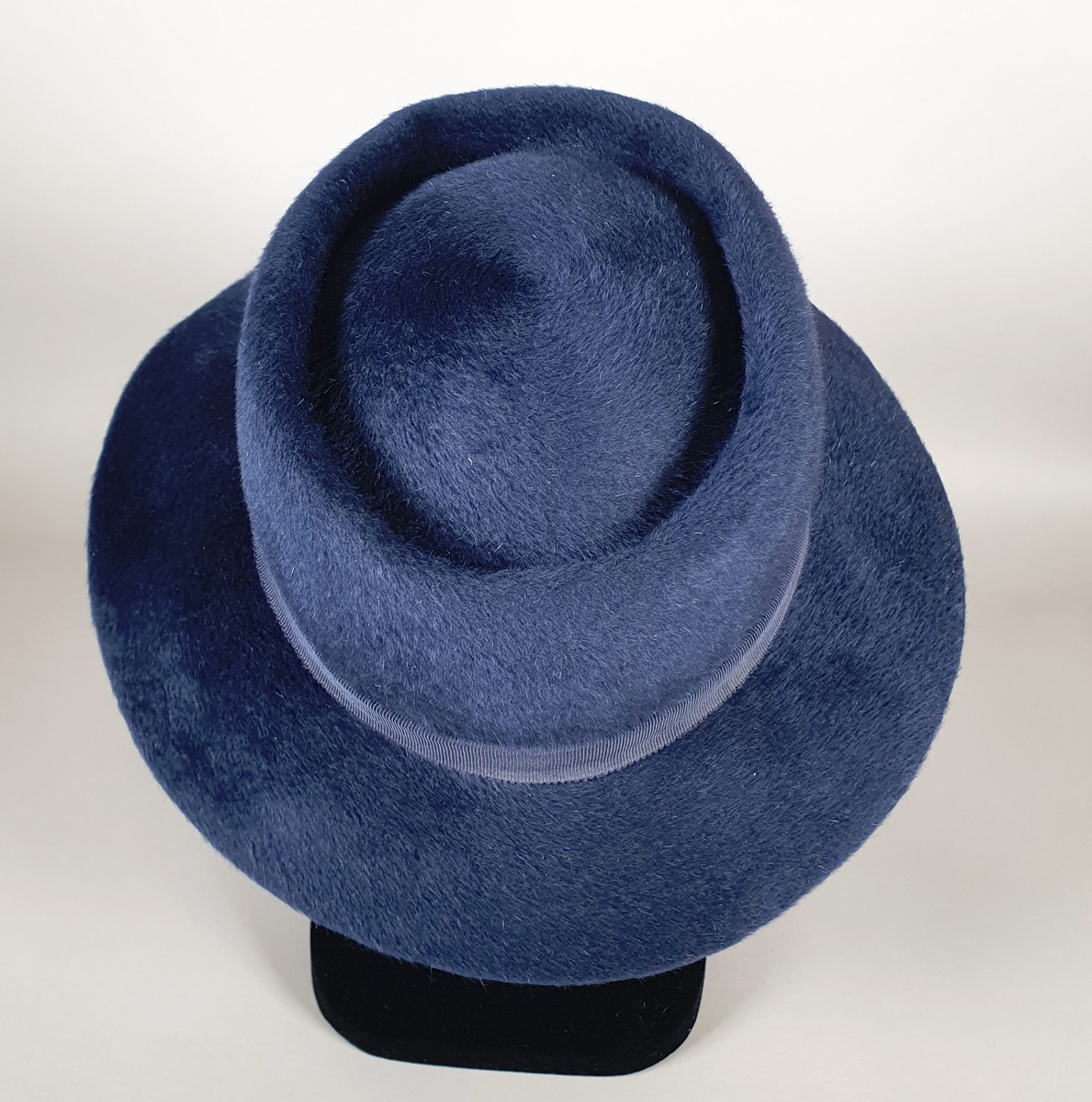 Blå hatt av børstet ull, med bred brem og blått ripsbånd rundt pullen. Blått ripsbånd på innsiden.