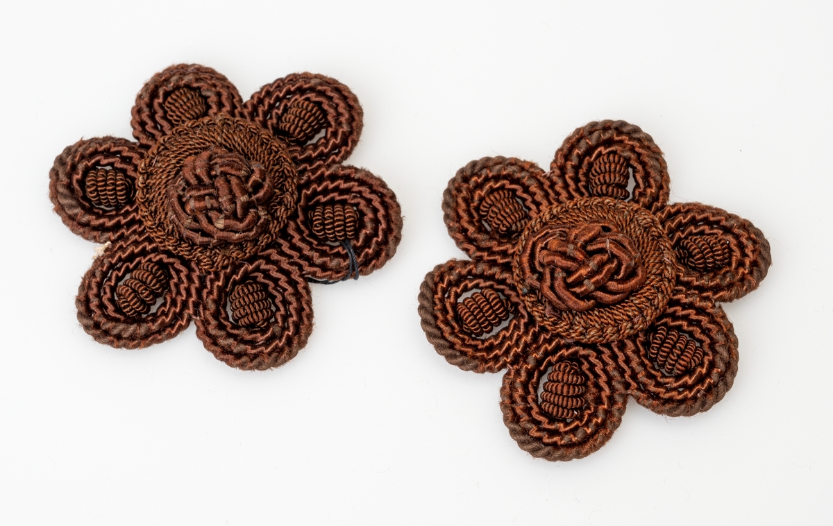 2 identiske rosetter brukt til møbler (møbelpossement). De er utformet som brune blomster. I midten er det en knute av silke og rundt er det seks kronblader av ull og silke.