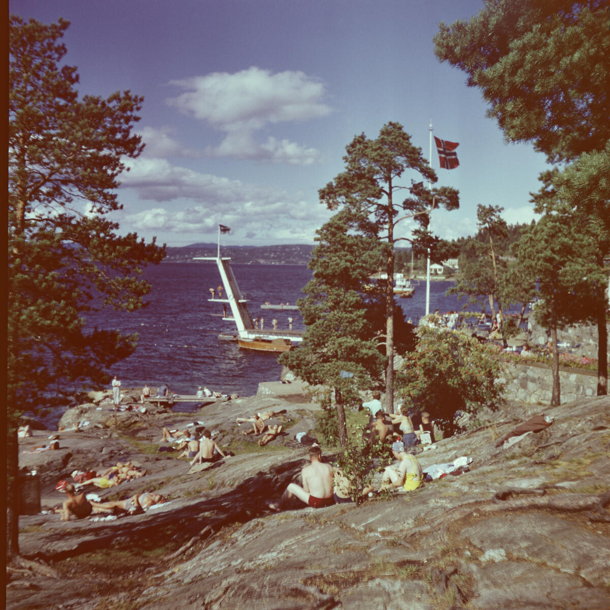 Bildet viser Ingiærstrand på 60-tallet. Landskap og badegjester som koser seg i solen. et stort flott stupetårn i bakgrunnen.