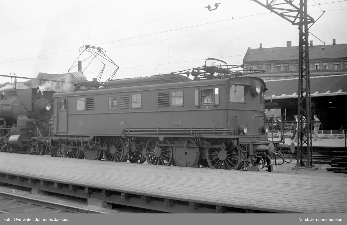 Elektrisk lokomotiv El 5 2035 som ekstra forspannlokomotiv i persontog til Trondheim, hurtigtog 1201, på Oslo Østbanestasjon. Til venstre damplokomotiv type 30b nr. 346 som forspannlokomotiv