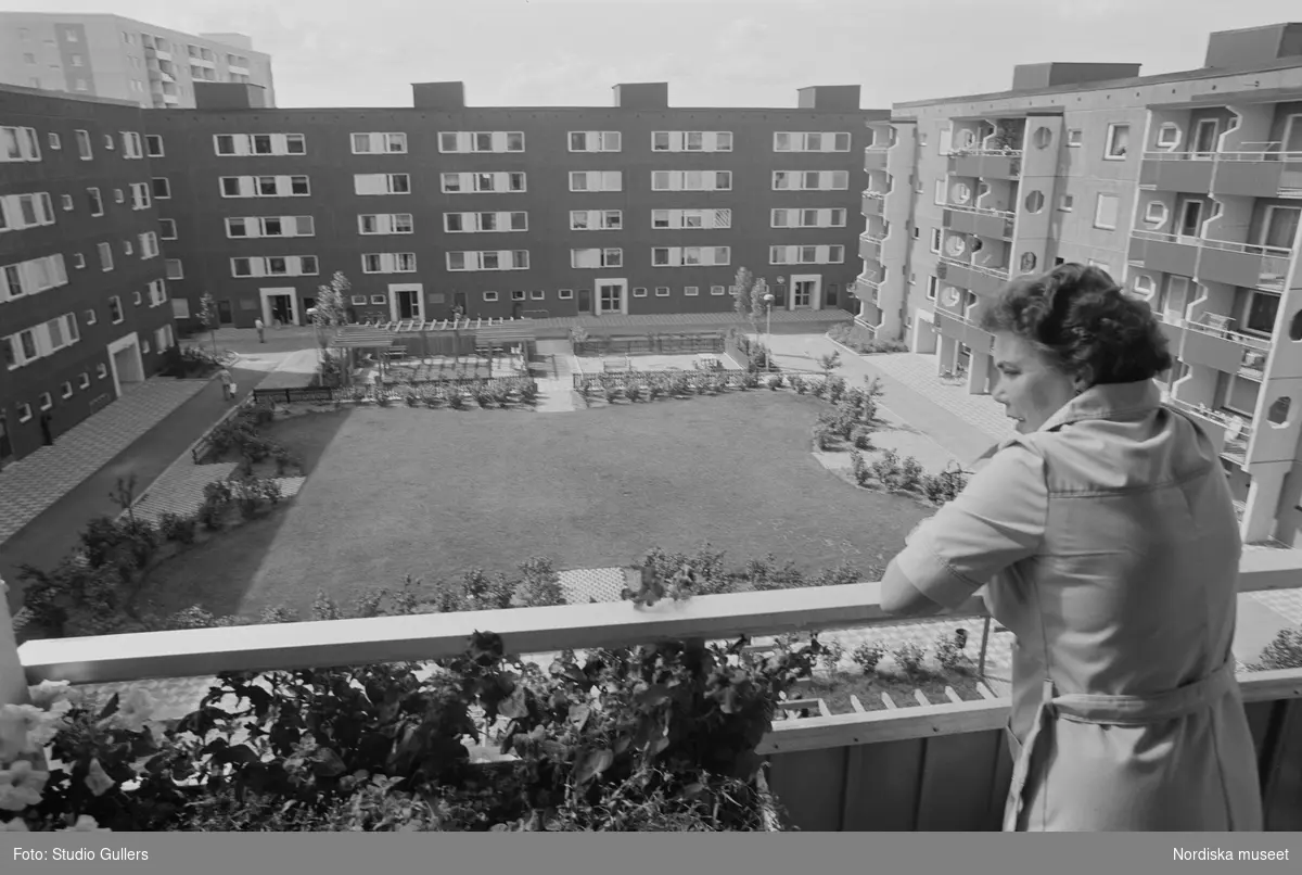 Tensta. En kvinna står på en balkong och blickar ut över en innergård och de fasader som omger den.