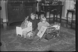 To barn leker på gulv i stue. Jenta sitter med en billedbok 