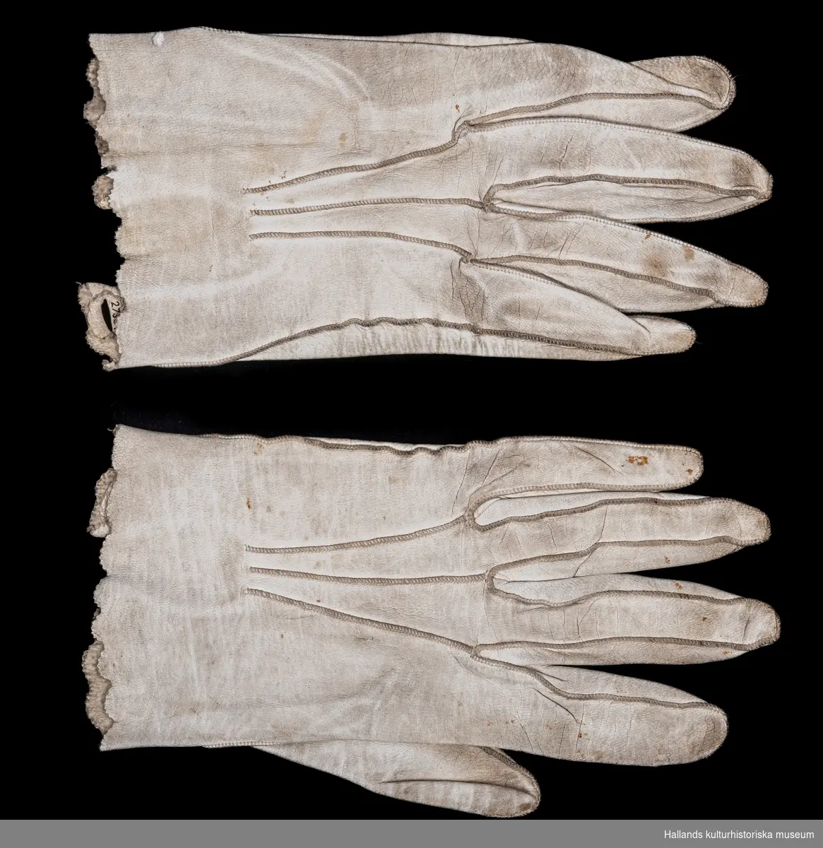 Två par bröllopshandskar av vitgarvat lammskinn. a-b) Herrhandskar. Längd 21 cm. c-d) Damhandskar. Längd 19 cm.