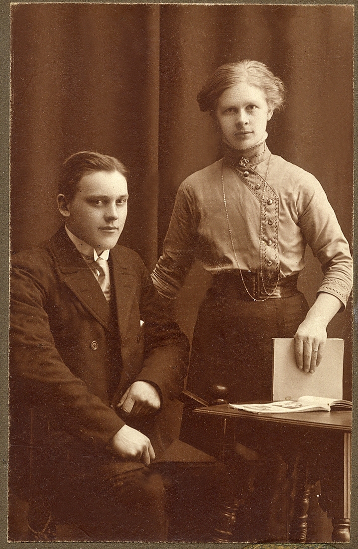 En man i kostym och stärkkrage sitter vid ett bord. Bredvid står en kvinna i höghalsad blus och kjol.
Under fotot skrivet med blyerts: "Anna o Hjalmar E.". 
Knäbild. Ateljéfoto.
