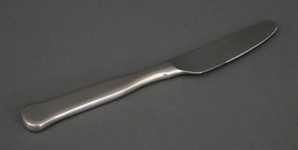Frokostkniv i presset rustfritt stål med smalt knivblad med små tagger. Skaftet tiltar i bredde og er rett frem til skaftenden som er bredere og avrundet.