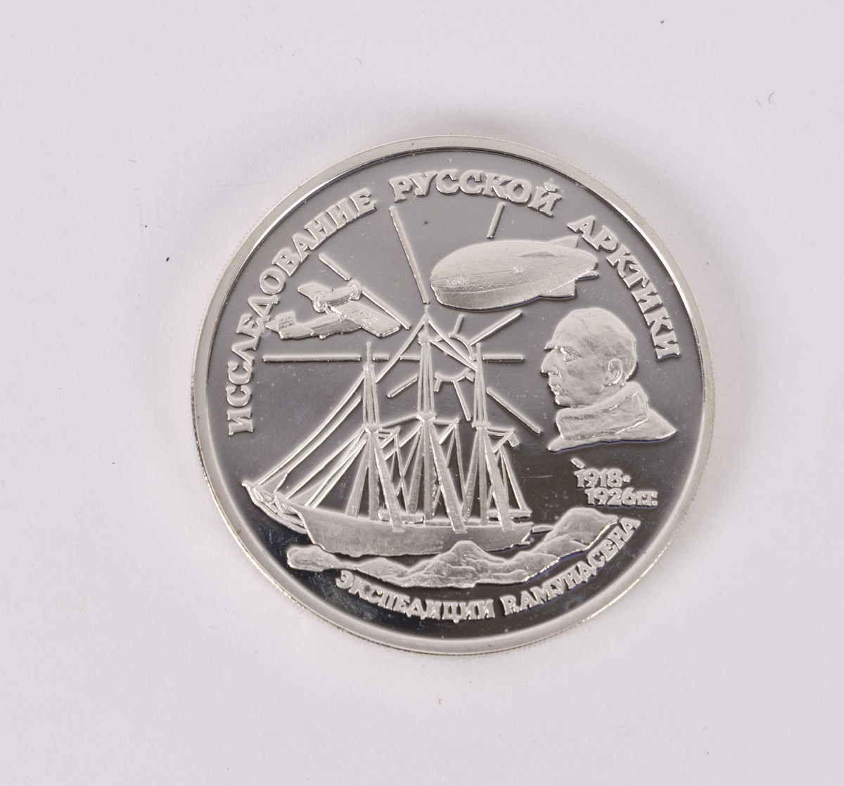 Myntens motiv forside viser Roald Amundsen og fremkomstmidler han brukte under polarforsking i Arktis. Bakside er en to-hodet ørn. 