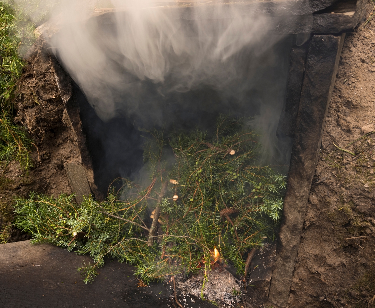 Fyring av røykovn under varmrøyking av røye under De nordiske jakt- og fiskedagene 2023 på Norsk skogmuseum i  Elverum, Hedmark, Innlandet. Det fyres med einerbar.