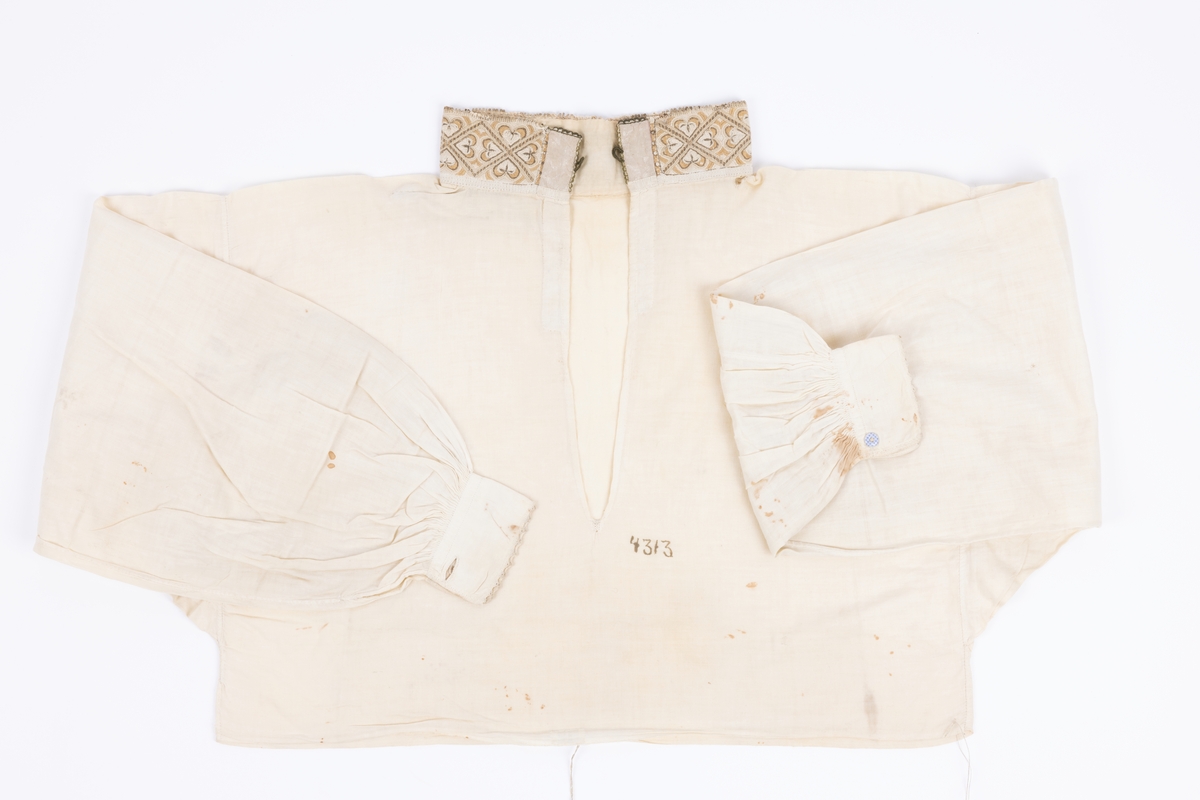 Skjorte brukt til belstestakk, kun broderi på halskvaren og hvite handkvarer med lite pynt. Sydd av tynt bomullsgarn.
Kvaren 6x41cm, senere forlenget framme med 2,5cm på hver side.