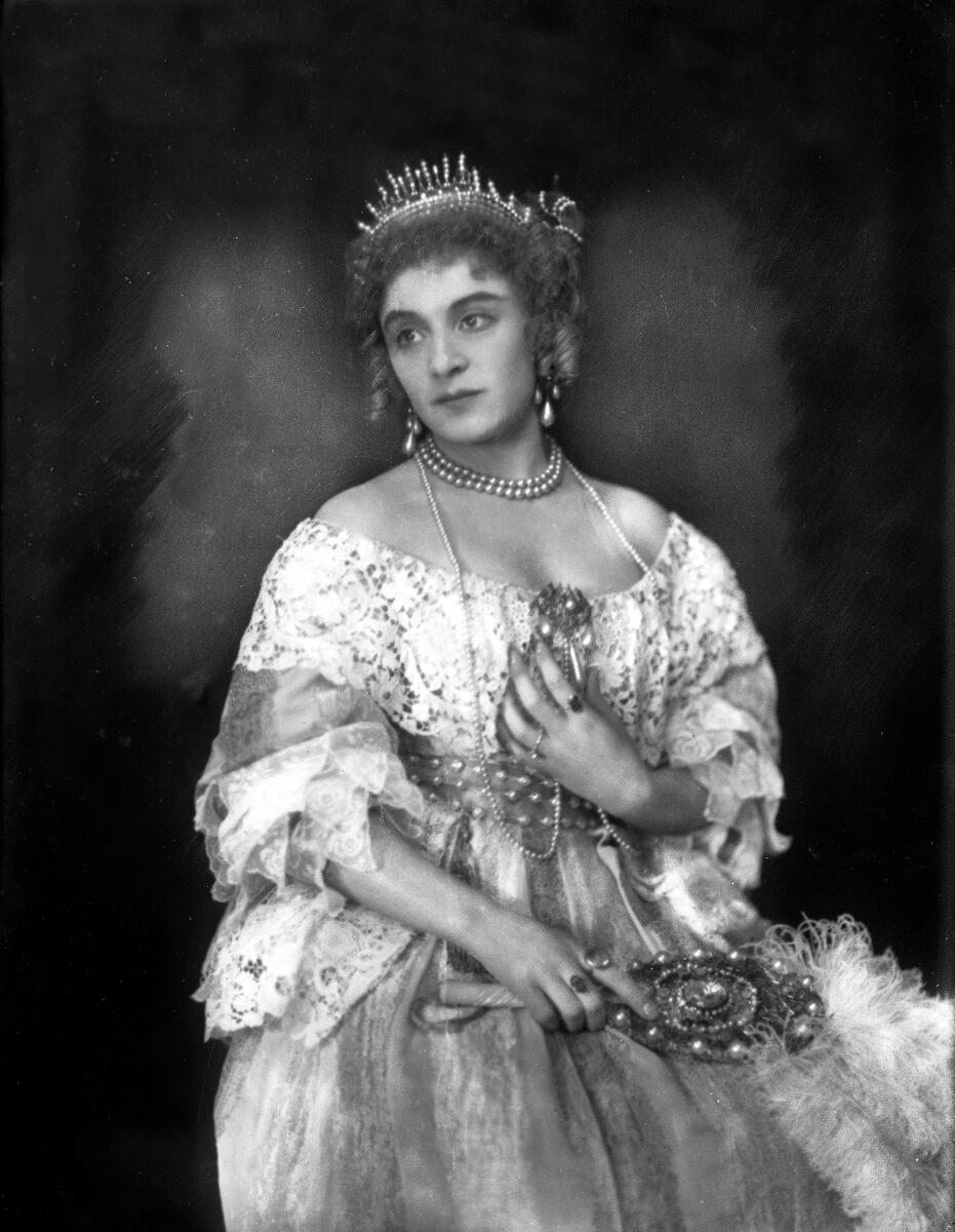 Portrett av skuespilleren og sceneinstruktøren Gerda Ring. Hun poserer sittende i en ballkjole. med en tiara på hodet og med diverse perlesmykker.