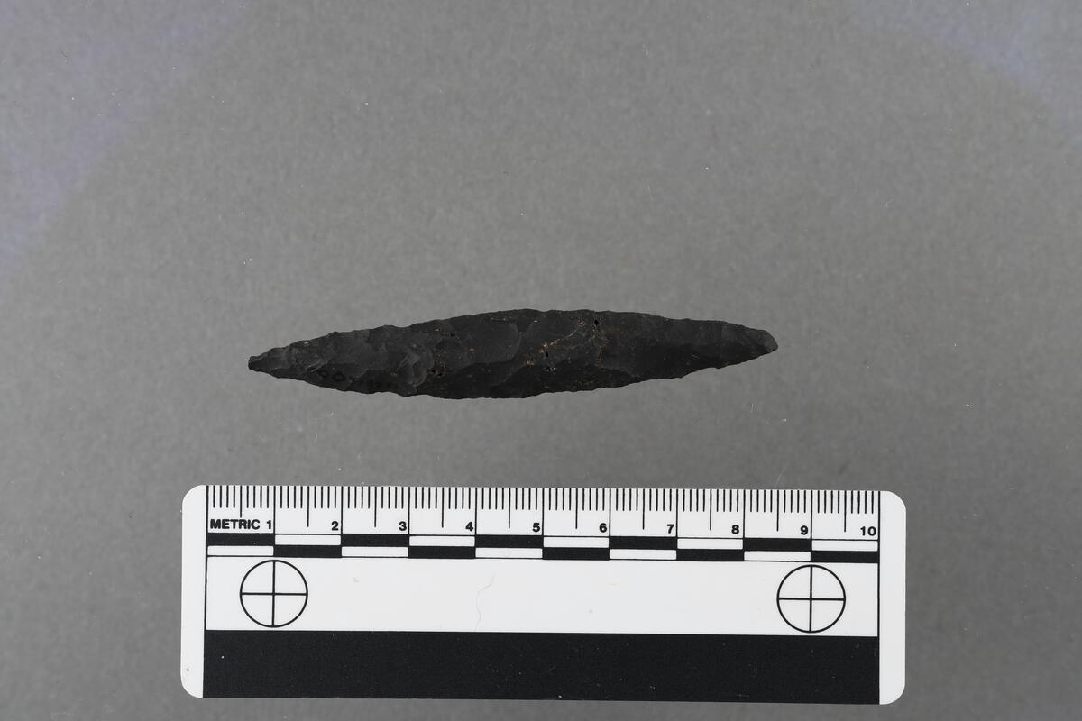 Tenformet pilespids af hornsten, af spidsovalt tværsnit, type Gj. 142. 8 cm l., 1,4 cm br., 0,8 cm t. Hel og vakker. (se fig.).
