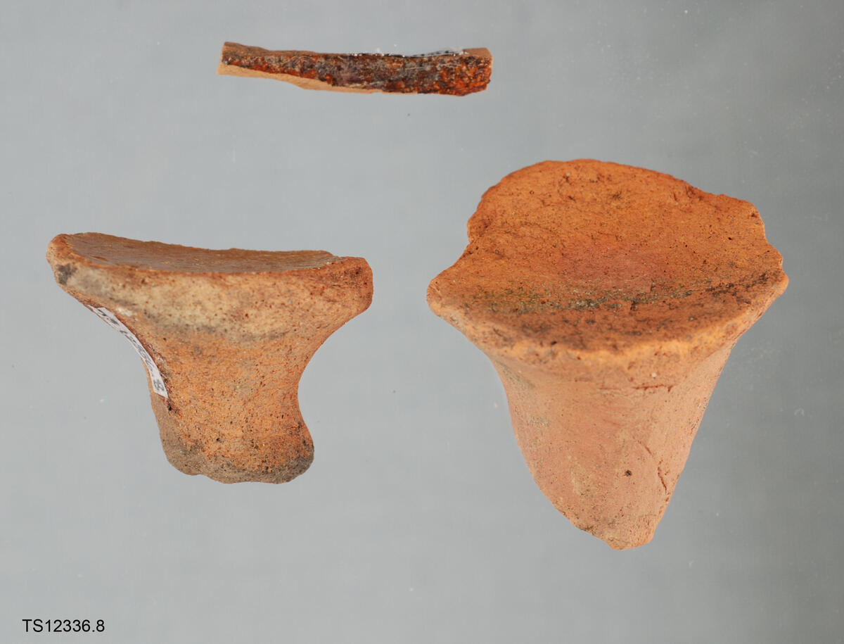 Tre (3) keramikkdeler. Rødt leirgods. To av delene antageligvis del av stjertpotte, da føttene. Evt. stett eller hankdeler.
Den tredje delen er et tynt langt fragment, med glasur.
LokalitetsID: 263197 