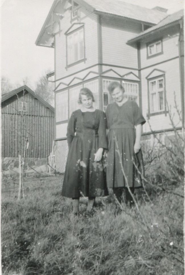 Systrarna Astrid (1907 - 1994, gift Jägerström) och Ingeborg Gustafsson (1901 - 1987, gift Johansson) står utanför hemmet, Kållered Stom "Nygård", 1920-tal. Deras föräldrar ägde gården.