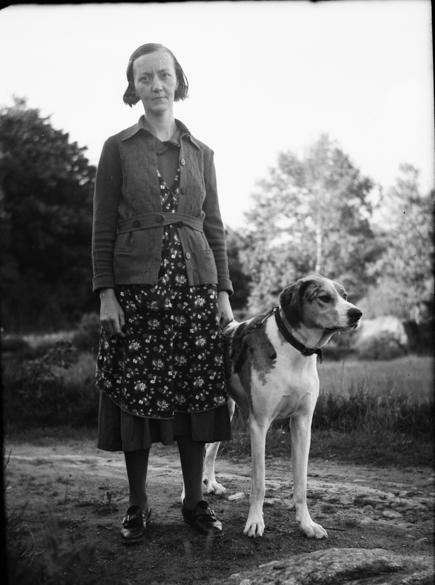 "Husa-Karls" dotter står utomhus med en strävhårig stor hund och håller i kedjan som är fäst i halsbandet.