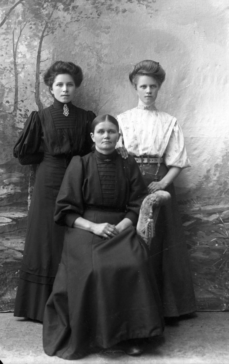 Atelierfoto.Gruppebilde (familiebilde?).En eldre kvinne og to yngre kvinner.