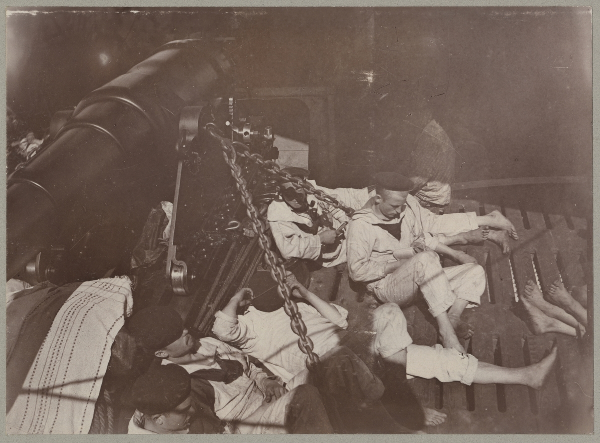 Fem sjömän vilar ombord på Balder bredvid en kanon. De bär vita sjömanskostymer och är barfota. En pojke läser en bok, en annan röker pipa och de tre i förgrunden sover middag.