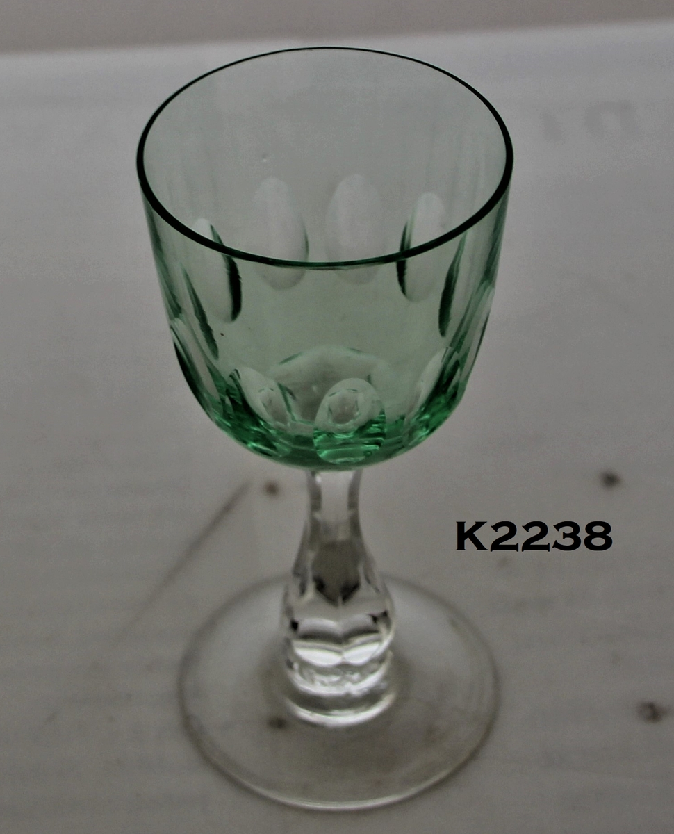Rhinskvinsglass:
Fot og stett av klart glass, cupa av lyst grønt.
Flat fot, stett med fortykket midtparti.
Rund, vid cupa med en rad olivenslipninger langs midten.
Hører til servise K 2239 og K 2240.