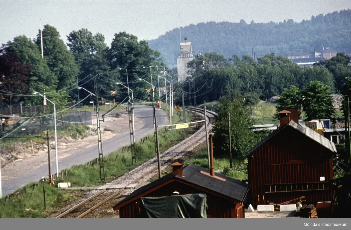 I förgrunden till höger ses järnvägens två hus strax söder om Mölndals Nedre station på 1970-talet. Industrispåret upp till Papyrusområdet, I fonden ses Sabematornet vid dåvarande Skedegatan (som inte längre finns). I bakgrunden ses Astra.