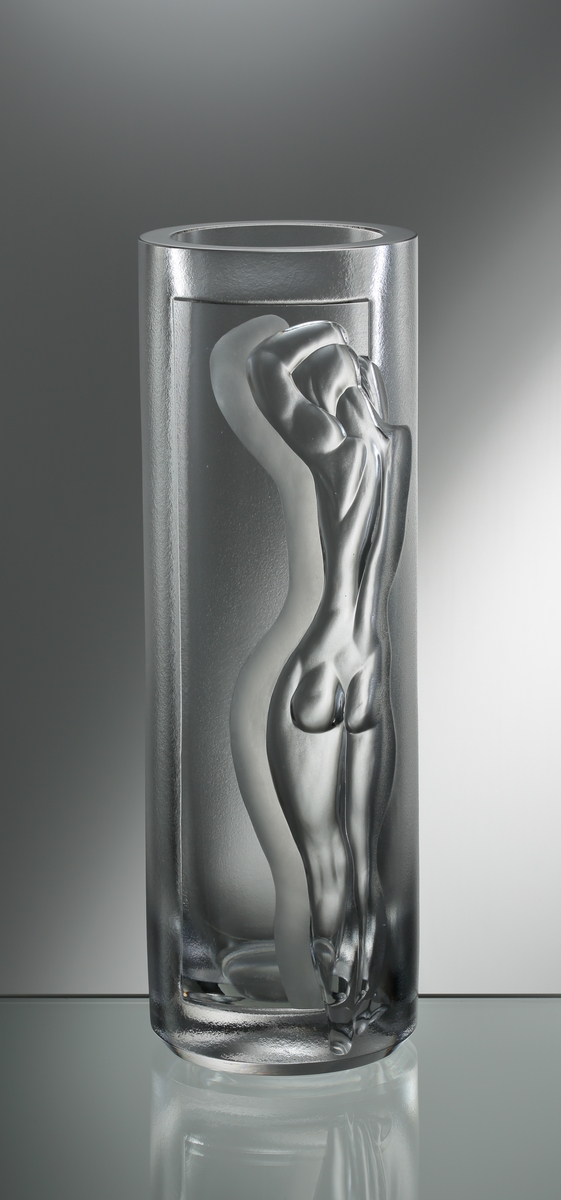 Formgiven av Vicke Lindstrand. Cylindrisk tjockväggig vas med slipat figurmotiv i form av naken kvinna.