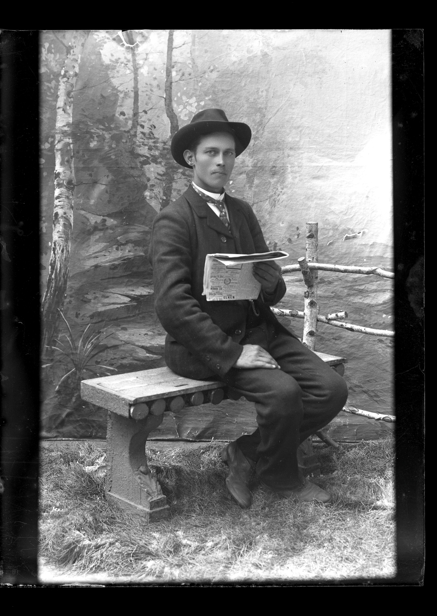 Atelierfoto. En mann sitter på en benk og leser i avis.