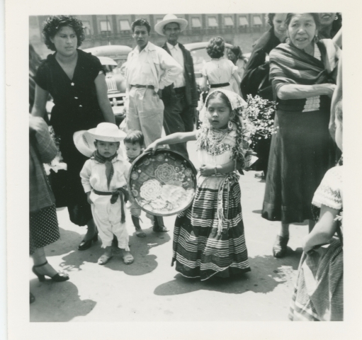 To barn i kostymer står sammen med en gruppe voksne. Barneparaden, Mexico. 