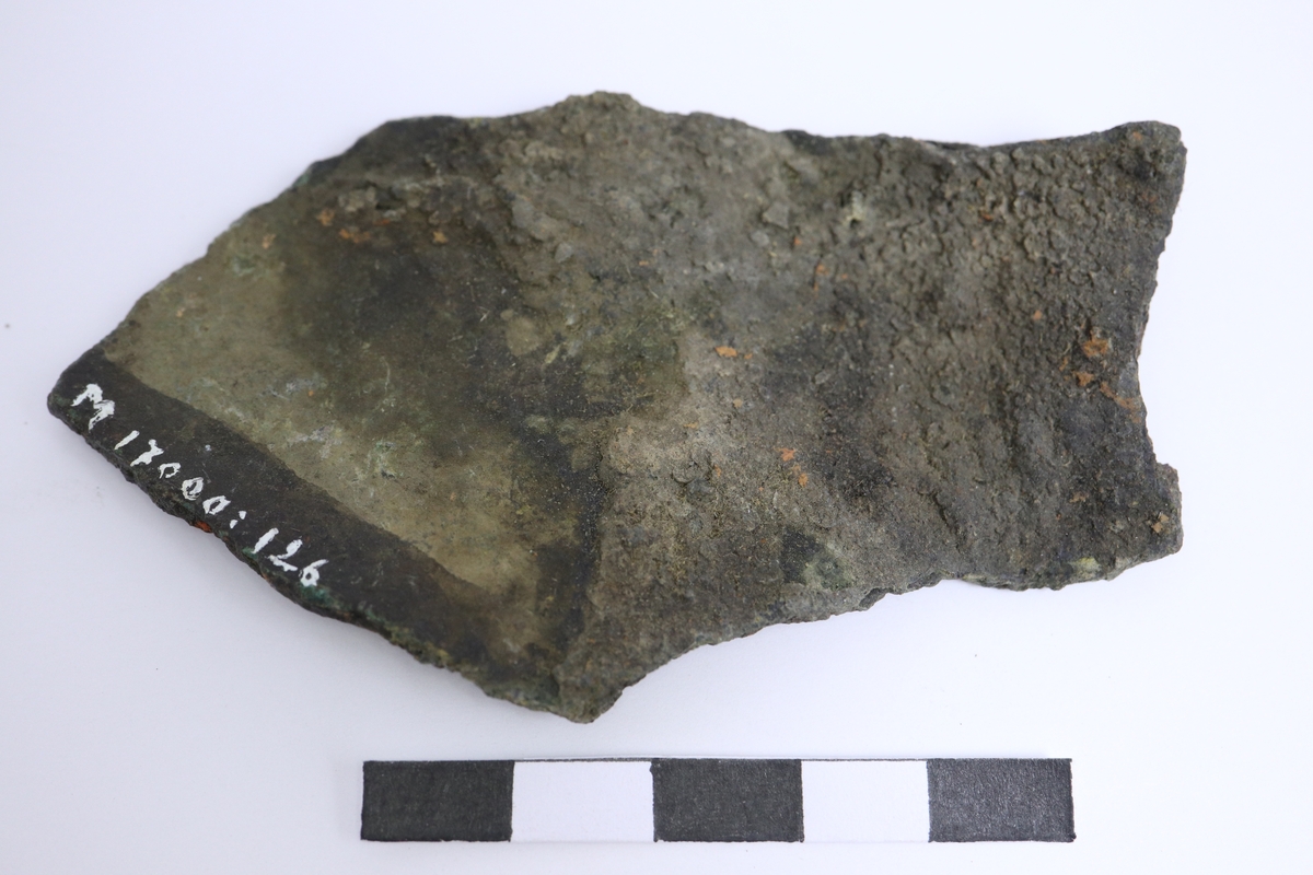 Brandskadat fragment av bronsgryta. Bukbit.