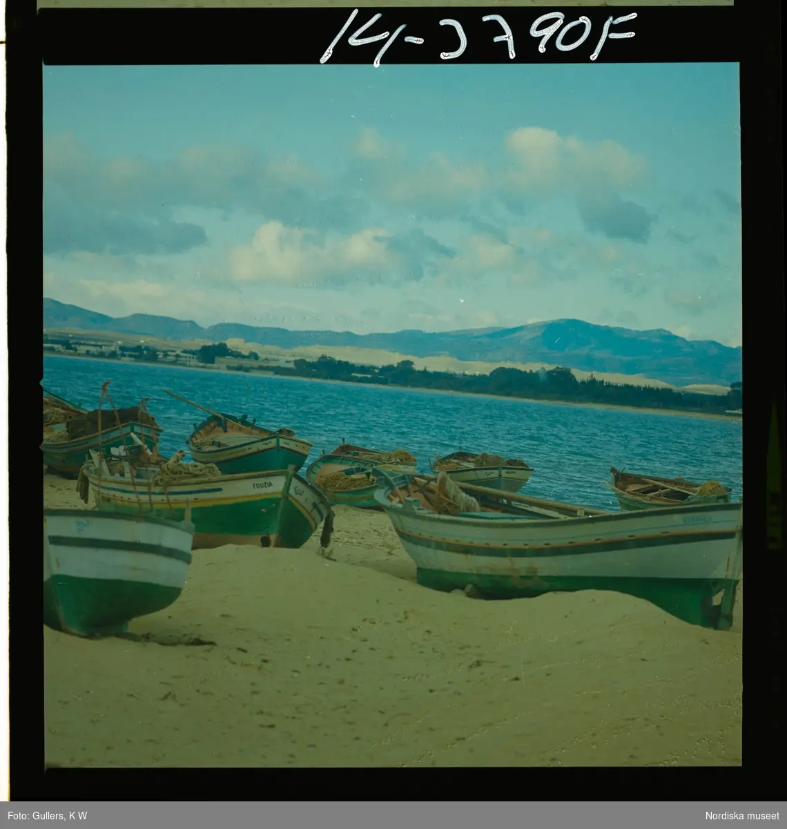 2791 Tunisien Kartago. Målade båtar på strand, vy över bergigt landskap.
