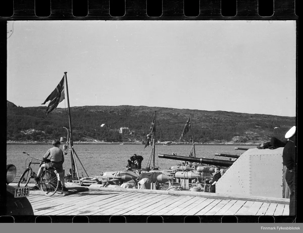 Foto av krigsskip i Kirkenes

En gutt sitter på sykkel og ser på skipene fra kaia

Nederst til venstre kan man se frontlykten av en bil med skiltnummer Y-3193

Foto trolig tatt på slutten av 1940-tallet, eller tidlig 1950-tallet