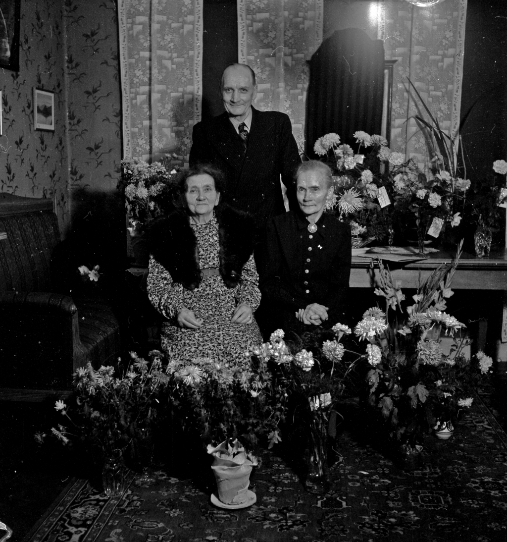 Tre personer samlade vid blomsterbord.