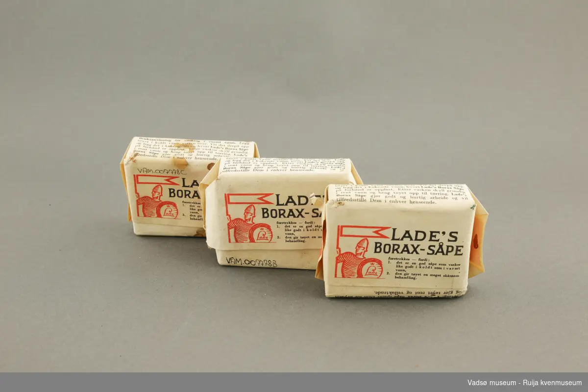 Tre pakker med Lade's boraxsåpe. Såpestykkene er pakket inn i papir. Såpen er ment til å vaske klær. Pakken er illustrert med en Laderidder/soldat på baksiden.