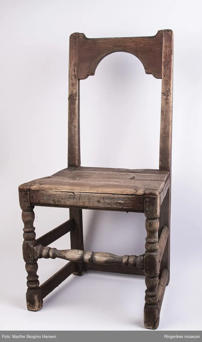 Trestol med åpent ryggbrett, toppstykket er halvsirkelformat i nederkant og rett i overkant, og dreide forbein. Antakelig fra 1700-tallet.