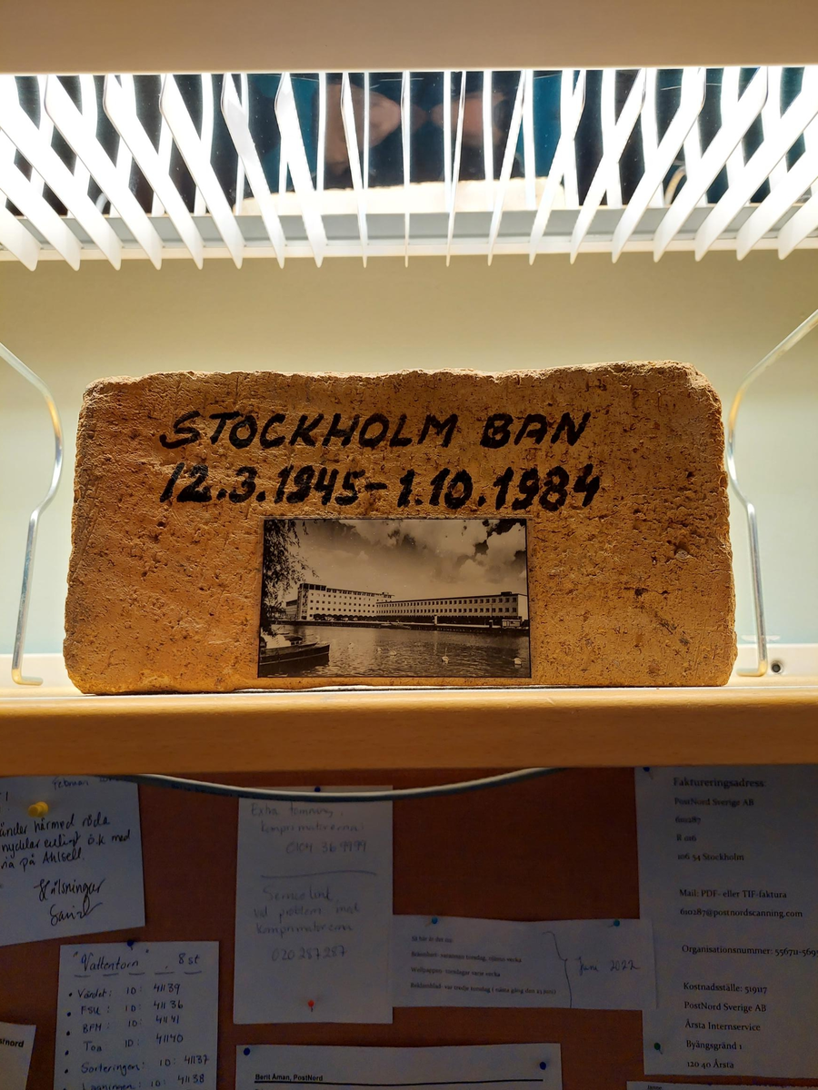 En tegelsten från Stockholms Bangårdspostkontor (Lellerstedts hus)
På ena sidan av tegelstenen text och påklistrat svart-vitt fotografi av fastigheten.