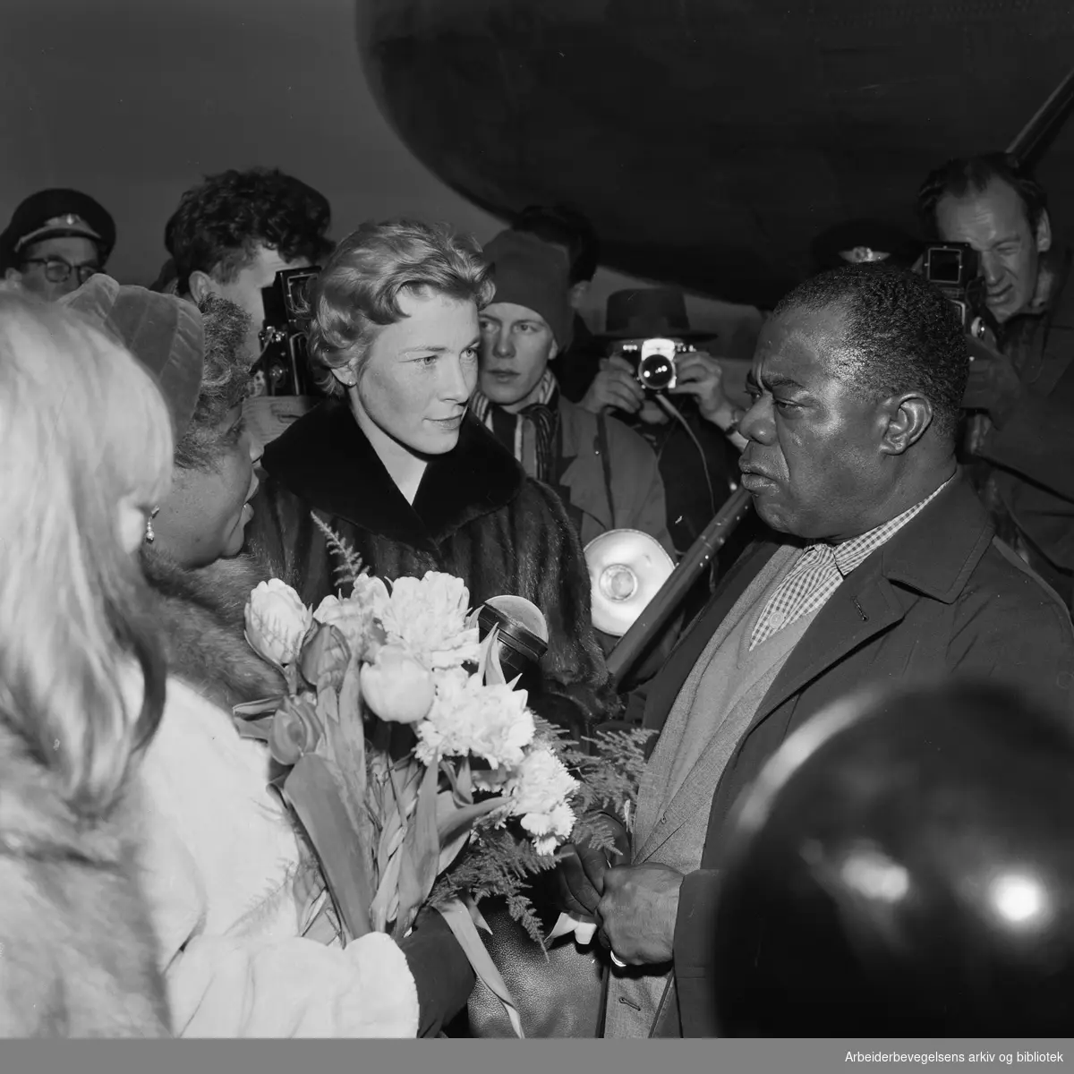 Louis Armstrong ankommer Oslo via Fornebu flyplass 2 februar 1959. Fra venstre: Lucille Wilson (hans kone), nrk-reporter Unni Børde og Louis Armstrong.