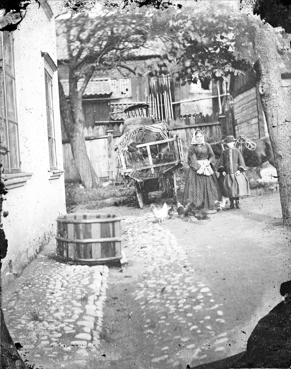 En kvinna och en flicka på en innergård, kvinnan matar höns, Uppsala före 1900