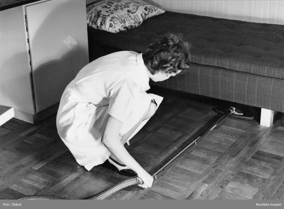 Städning i ett rum. Kvinna dammsuger under säng. Troligen Hemmens Forskingsinstitut (HFI).
