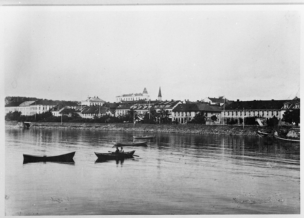 Fire robåter, og i kanten til høyre kan vi se forparten på ei jakt.  I bakgrunnen ser vi Strandgata på Hamar.
Postkort.