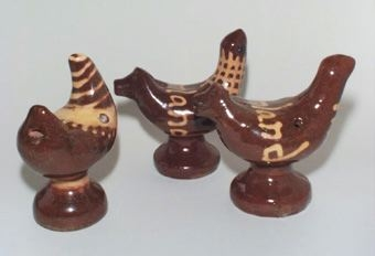 Bruna lergökar av lergods med tre toner. De tre fåglarna har olika typer av gult, hornmålade dekorationer. Två har dekor med text "Värmland" på ryggen.