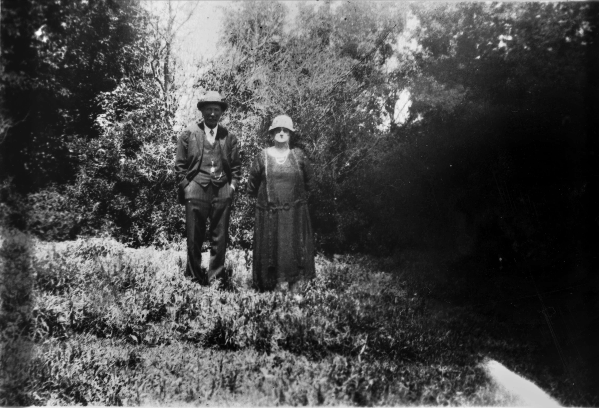 Portrett av mann og dame stående på gressmark, med skog i bakgrunnen.