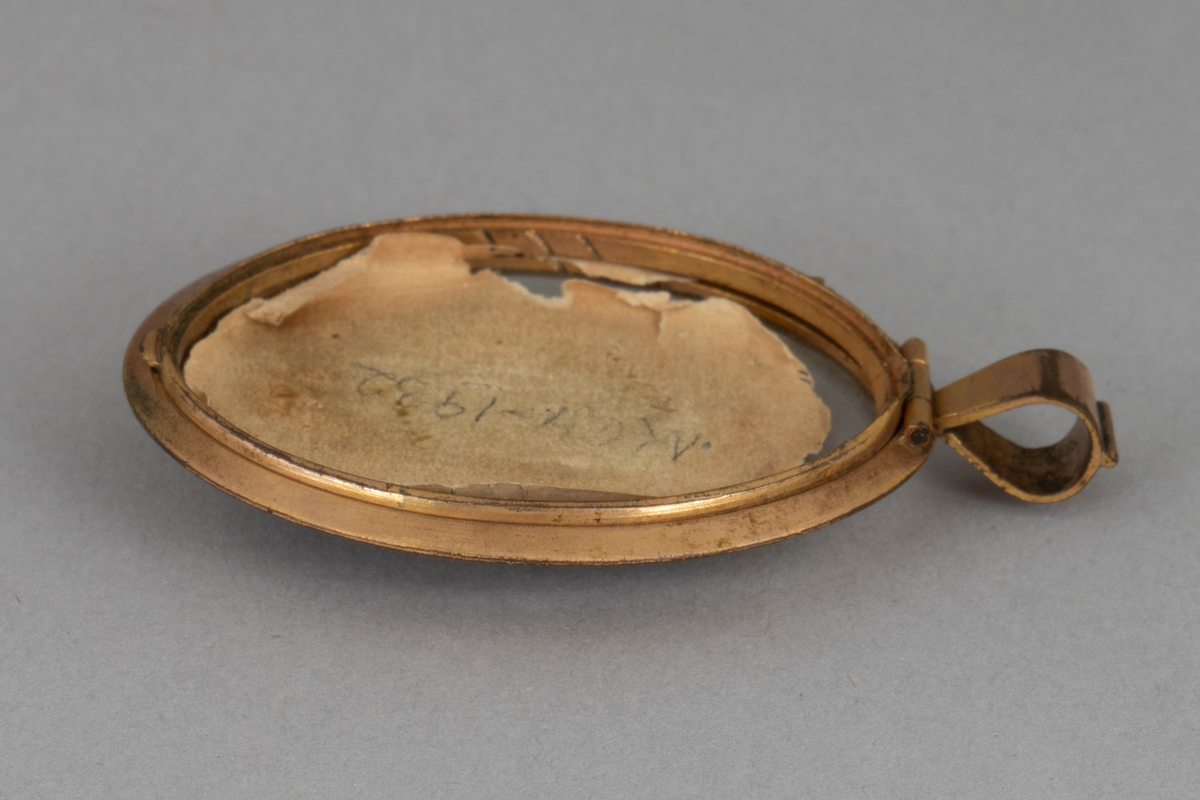 Ovalformet anheng/ medaljong bestående av et miniatyrmaleri av en prest i en ramme av forgylt metall med hempe øverst. Glass på forsiden, bakplaten mangler.