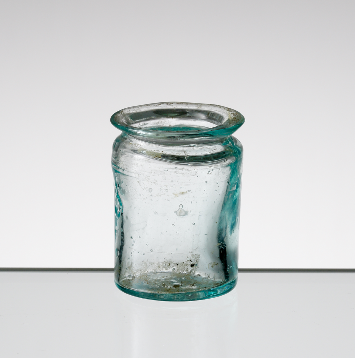Apoteksburk i blågröntonat glas från Hofmantorps glasbruk. 
Cylindrisk med utvikt mynning. Puntelmärke.
Siffran "15" i upphöjd relief på livet.