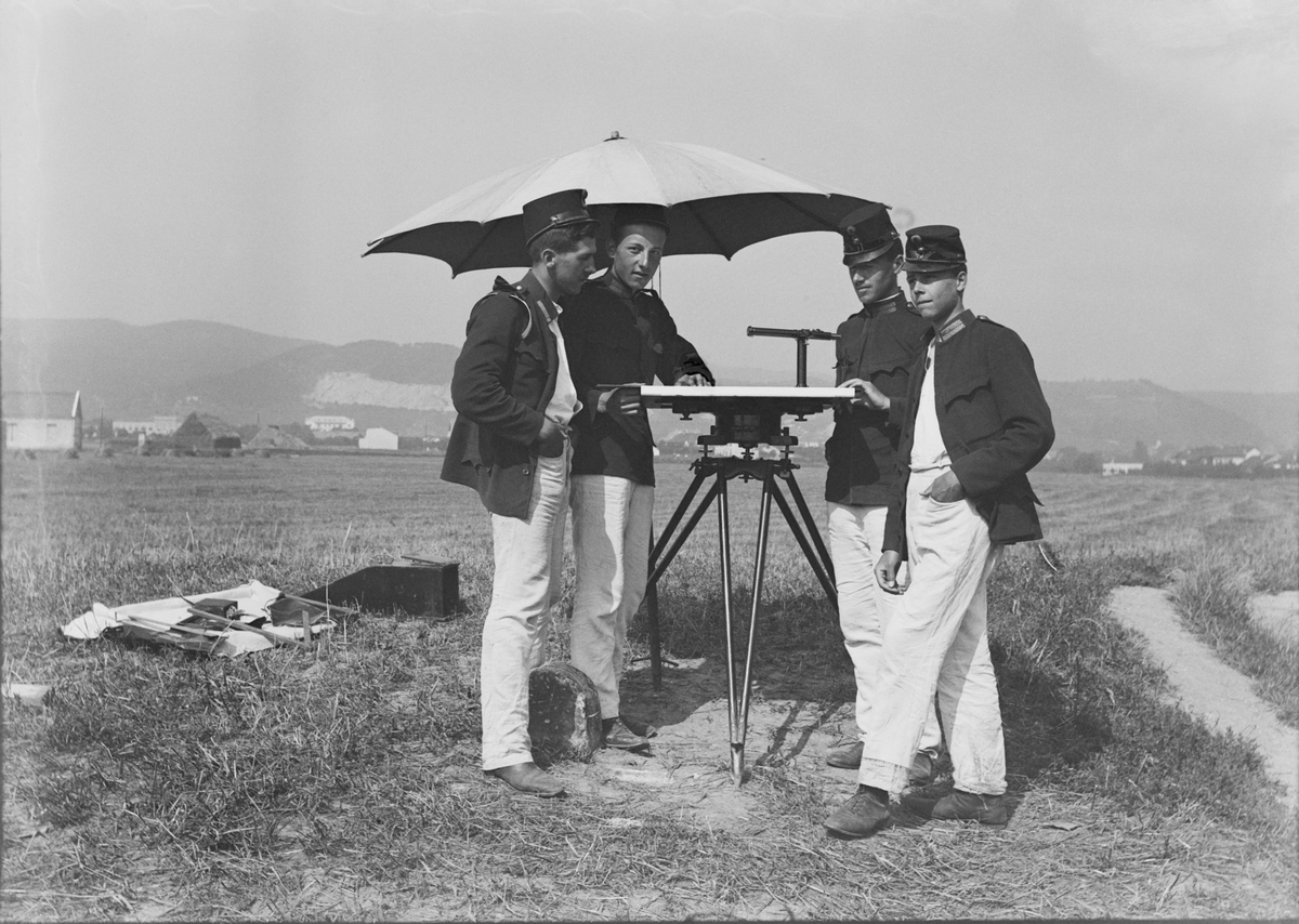 Fyra militärer från Österrike-Ungern står vid ett kartbord med instrument och parasoll på ett fält. Andra från vänster är Edmund Sparmann. Byggnader och höga berg i bakgrunden.