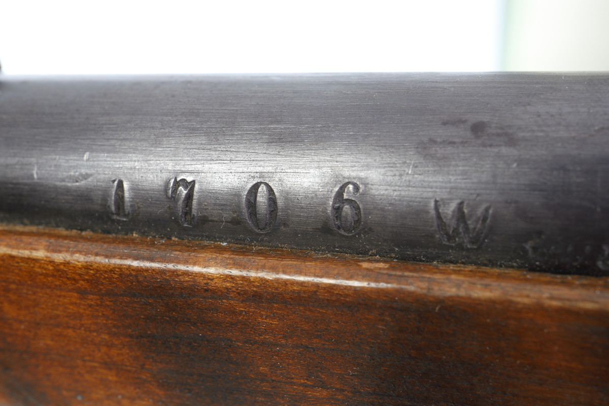 Armégevär omändrat till jaktgevär med mekanism av typ Remington Rolling Block, med centralantändning. Kolven har en smal kolvhals och bakplåt i mässing. Kolven är av halvstockstyp där framstocken slutar ca 495 mm. bakom mynningen. Lås och pipa är blånerade, och på pipan sitter ett uppfällbart sikte, och längs fram vid mynningen ett "T" format korn. Bärremmen är  vävd i grönaktig textil med förstärkningar av läder. Pipan är räfflad med en innerdiameter på 12,7 mm.
Inskrivet i huvudkatalogen 1967.
