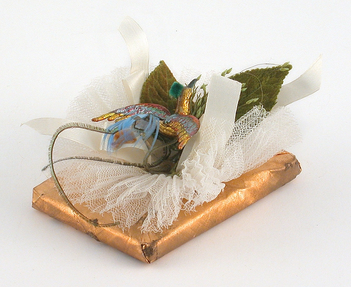 En sockerkaramell i guldpapper, prydd med ett lindebarn och en fågel i originalkartong.